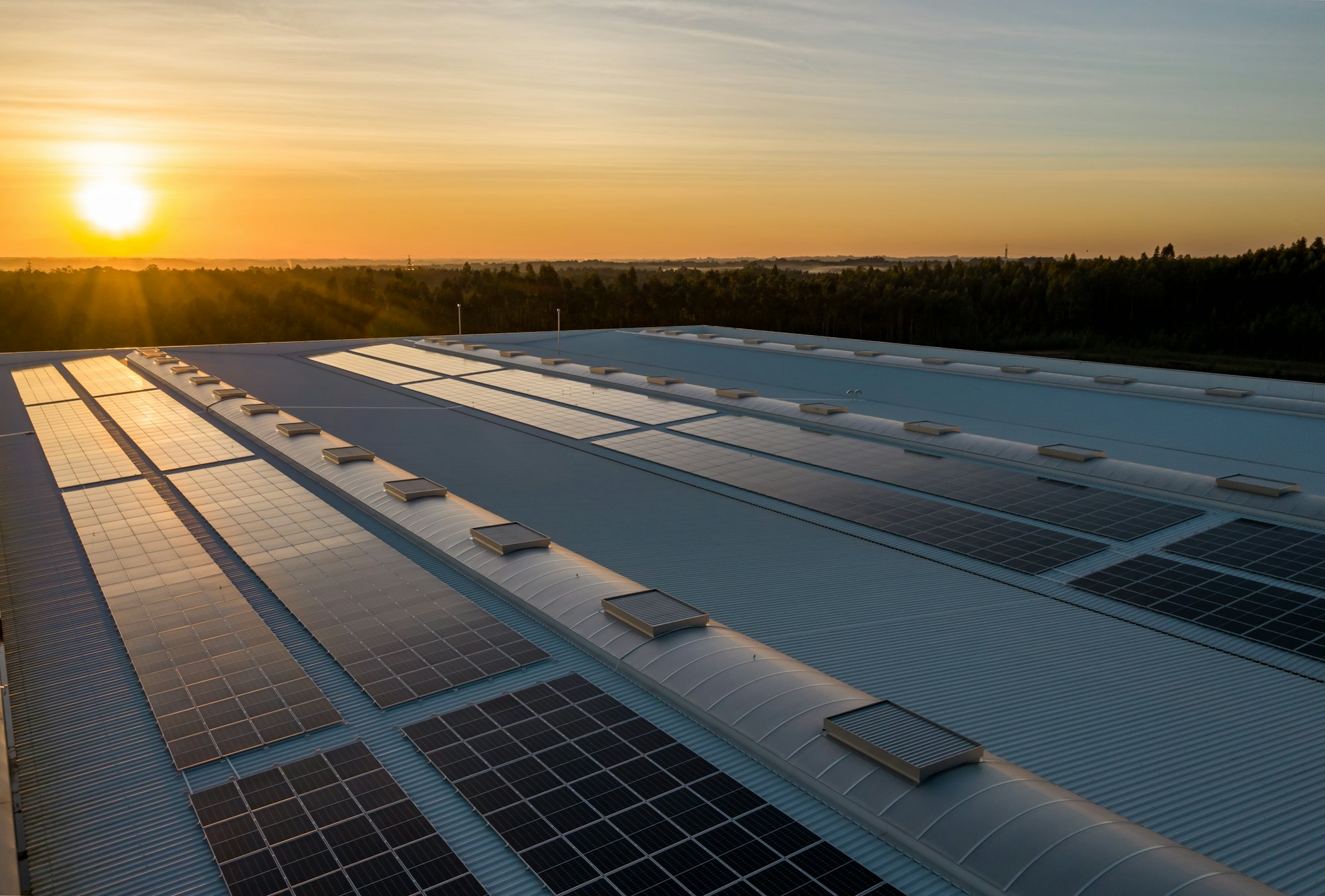 Placas solares instaladas no telhado de um galpão ao pôr do sol